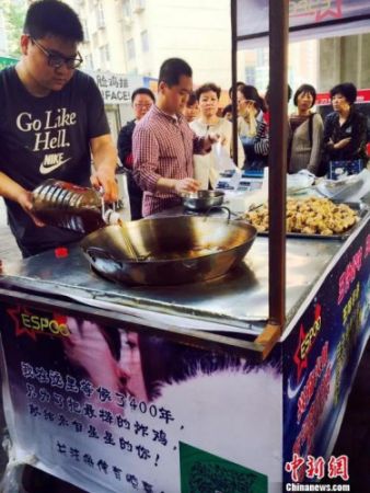 　　郭方正(左)正在往锅里倒炸鸡用的油，摊位边等待的顾客已排起长队。　曹铮 摄